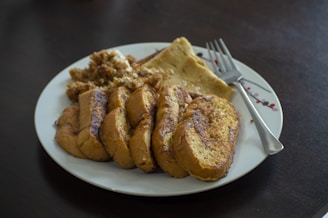 Hands holding a fork cutting into the soft egg nog French toast on a festive plate.