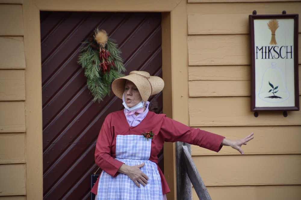 a woman in a dress and hat standing in front of a door