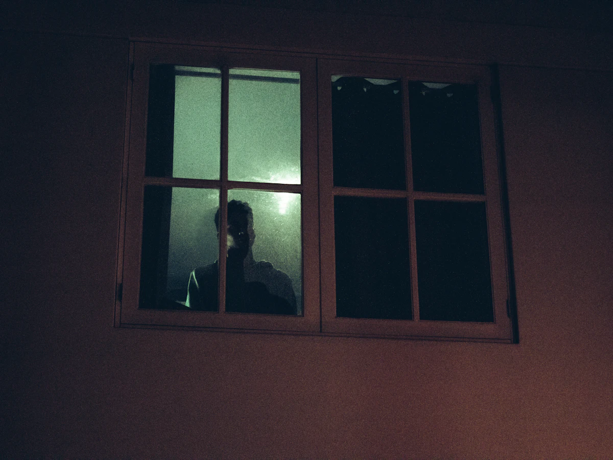 Person alone looking out of a window at night, representing the persistent isolation of depression