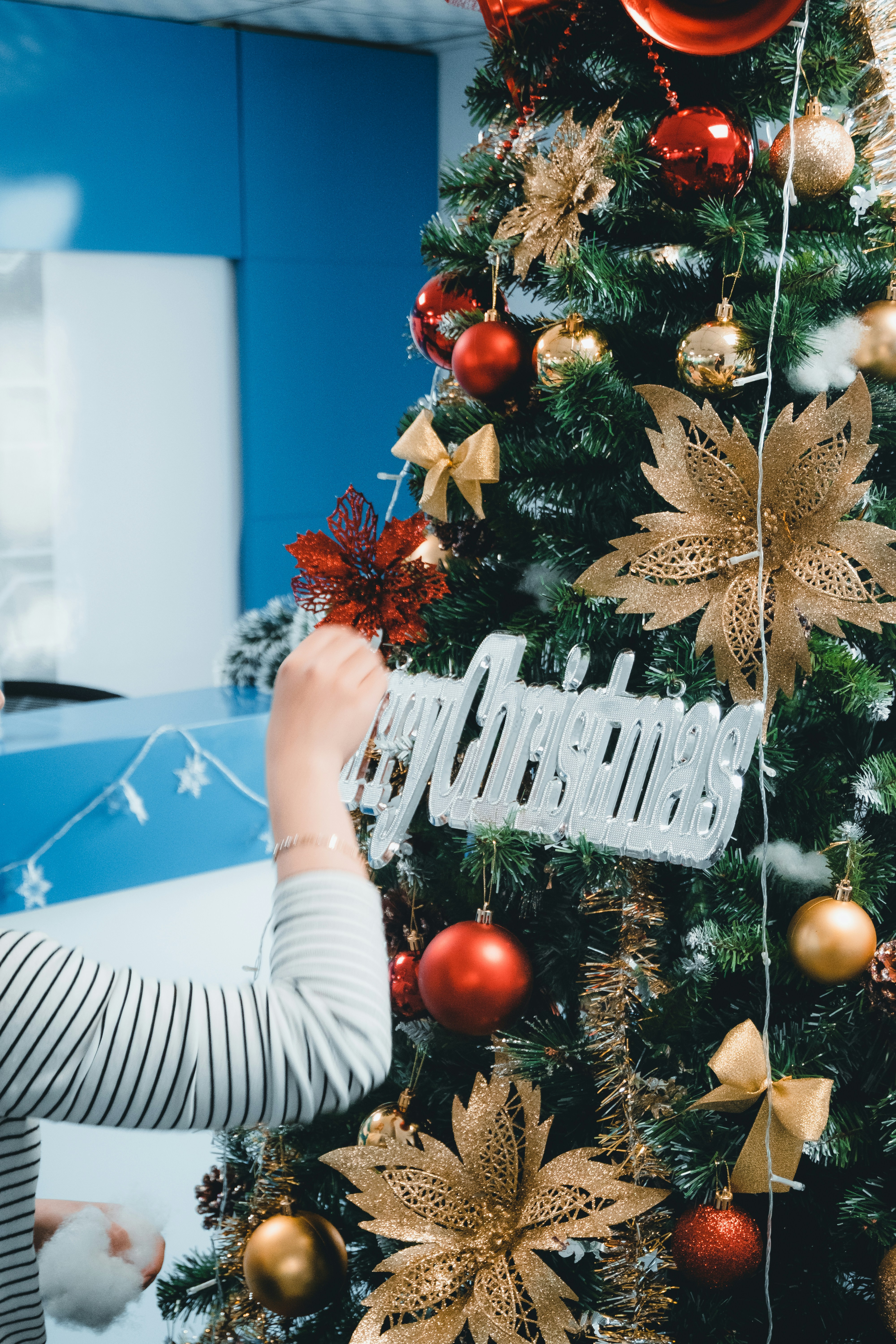 Una mujer decorando un árbol de Navidad con adornos rojos y dorados