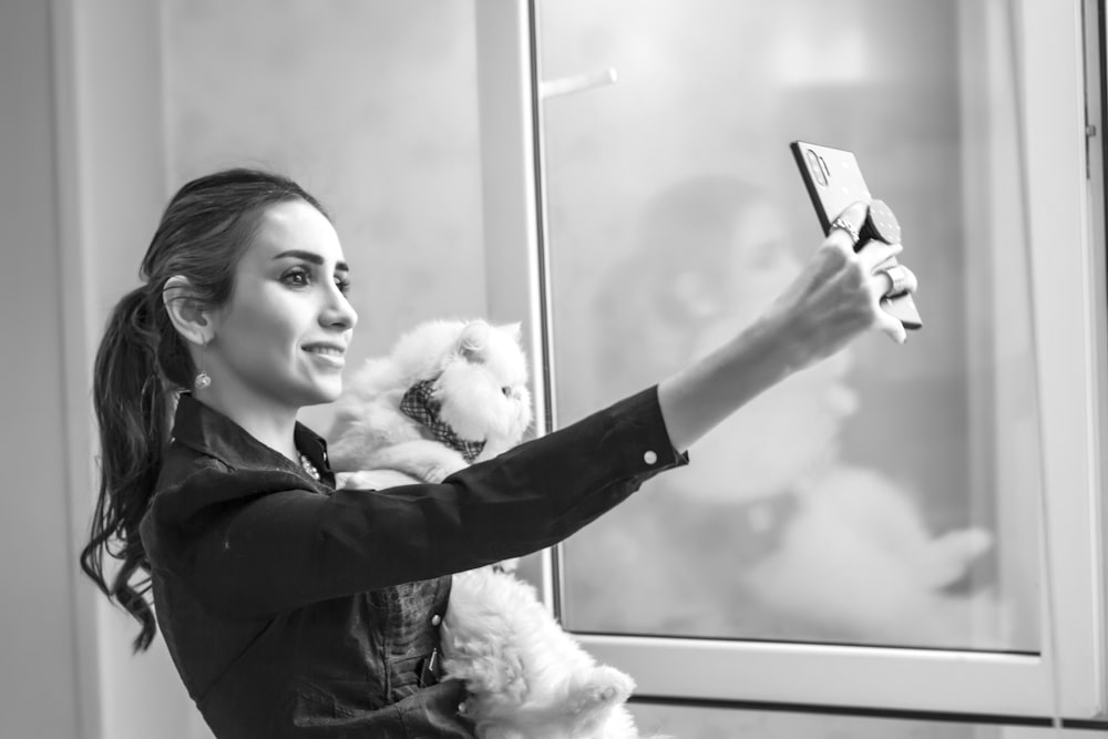 a woman holding a teddy bear and taking a selfie