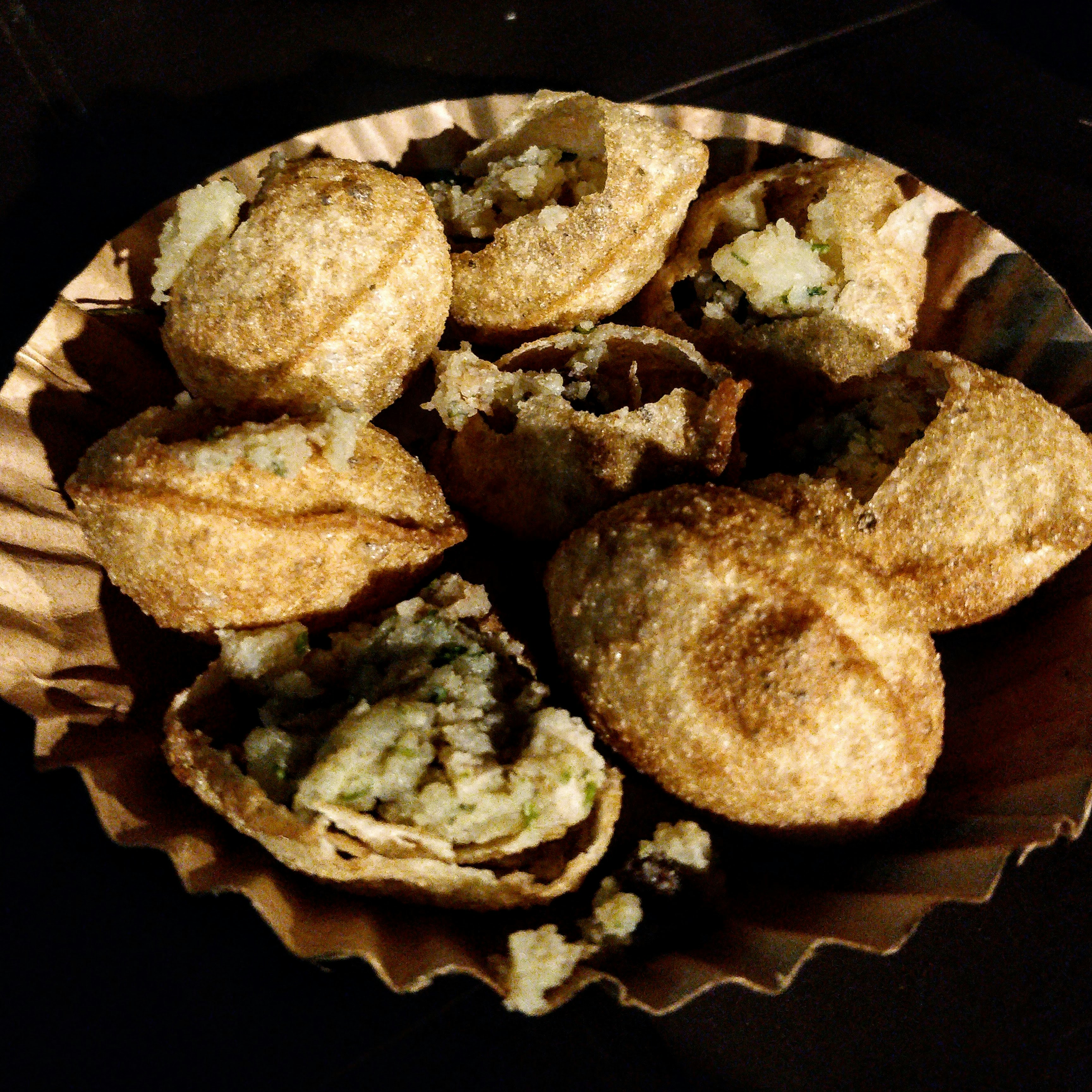 Crisp, hollow pani puri shells broken open and filled with a mashed potato and herb filling, on a fluted paper plate