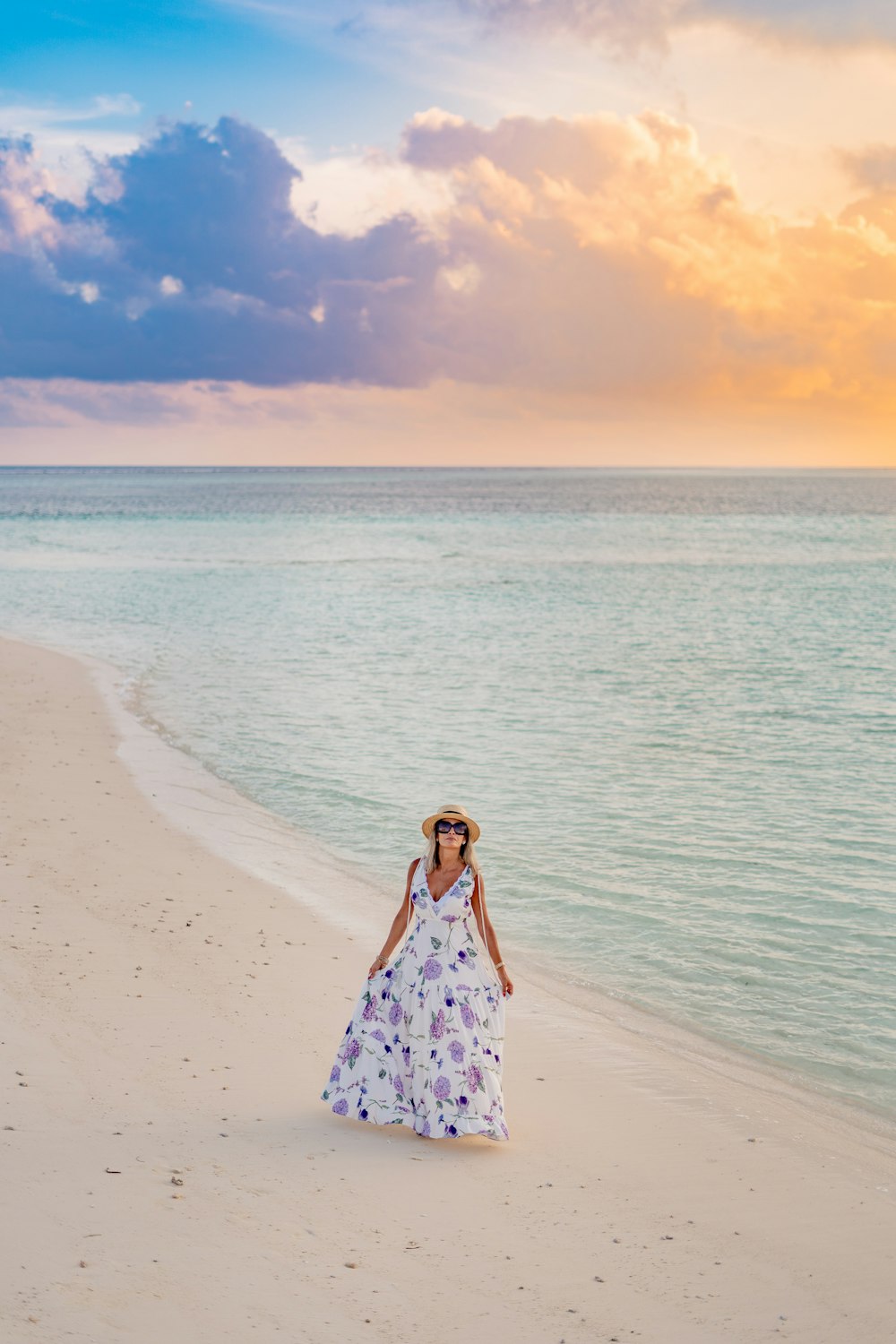a woman in a dress and hat walking on a beach