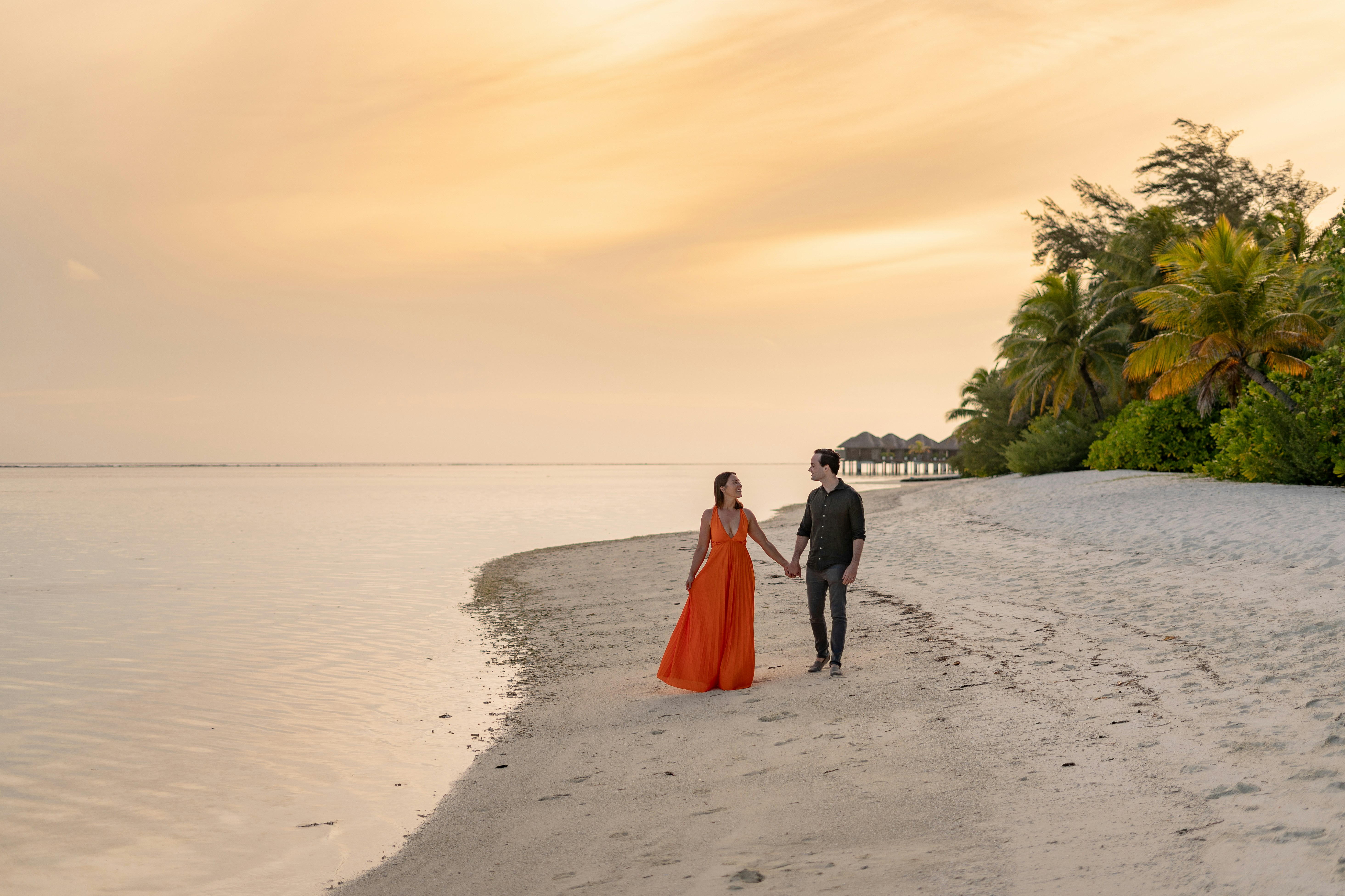 a man and woman walking on a beach holding hands, 