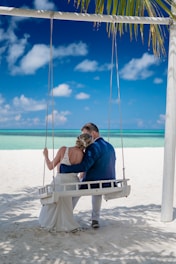 a bride and groom sitting on a swing at the beach