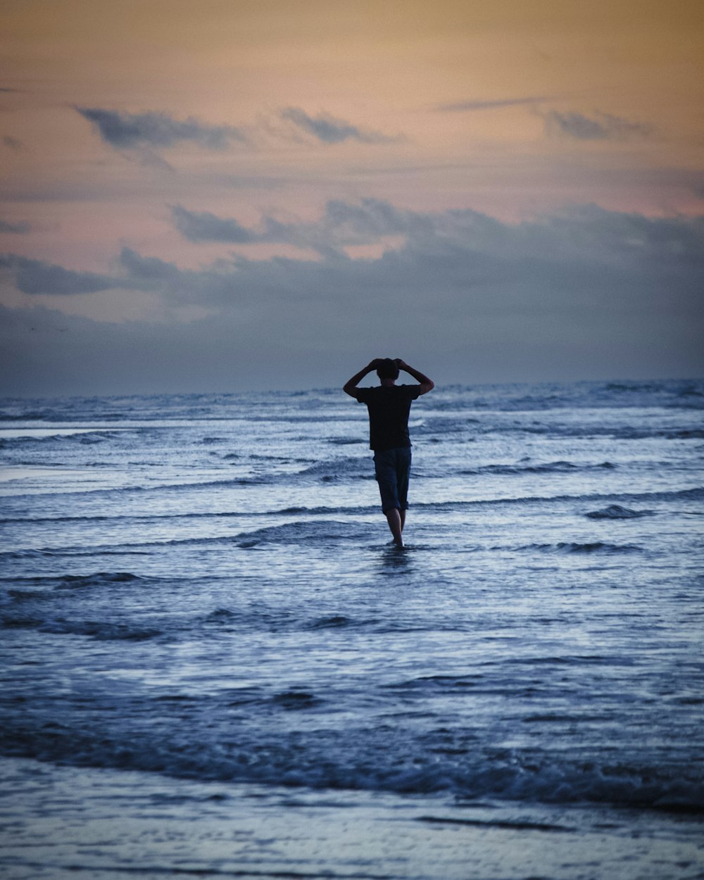 a person standing in the ocean with their hands on their head