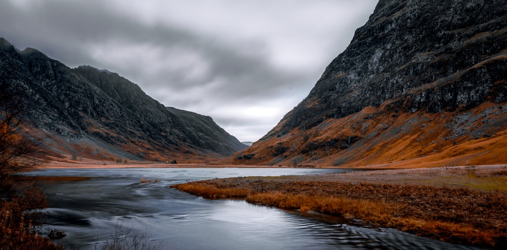 a body of water surrounded by mountains under a cloudy sky