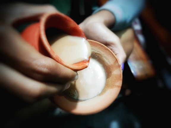 Hands gently pouring golden milk from a ceramic pot into a cup.