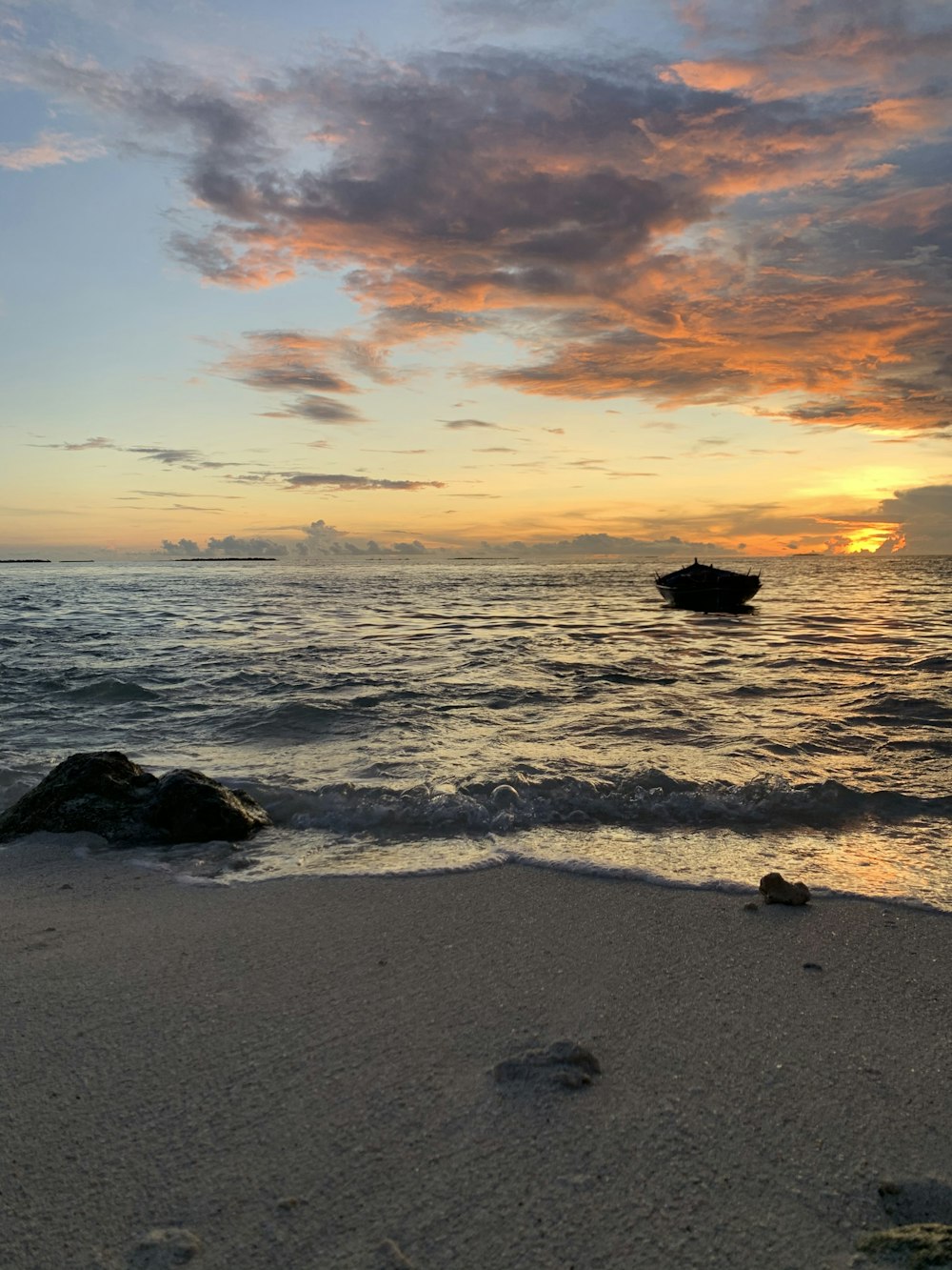 a boat in the water at sunset on a beach