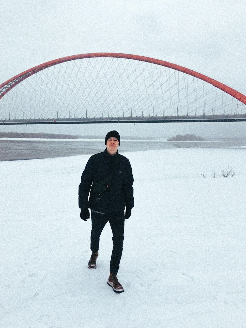 a man standing in the snow in front of a bridge