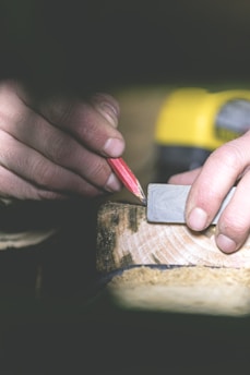 A close-up of a construction worker's hands measuring wood on a job site bathed in warm sunlight.