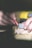 A close-up of hands holding a red carpenter's pencil and a gray measuring tool over a piece of wood. The yellow blurred background suggests a workshop environment.