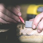 a person using a pencil to cut a piece of wood