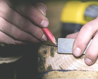 a person using a pencil to cut a piece of wood