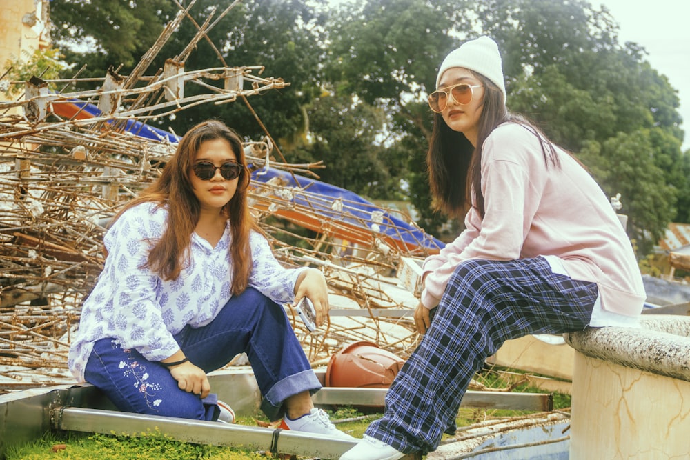 two women sitting on a ledge in front of a pile of junk