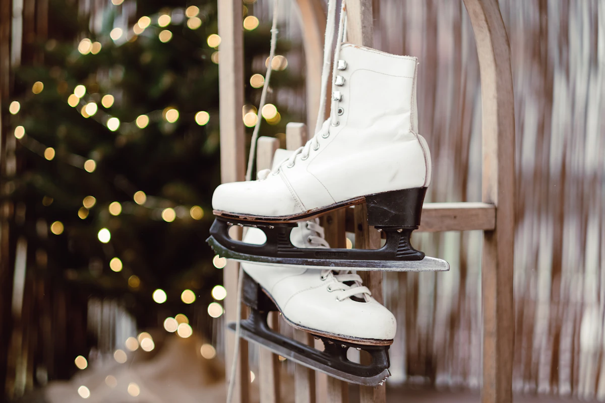 White ice skates hanging on a wooden rail against a background of lights
