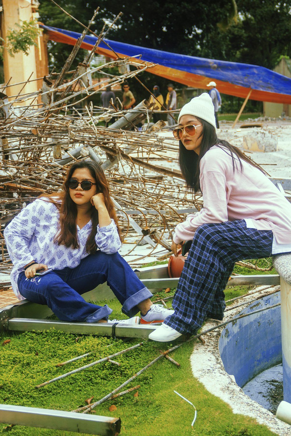 two women sitting on the ground in front of a body of water