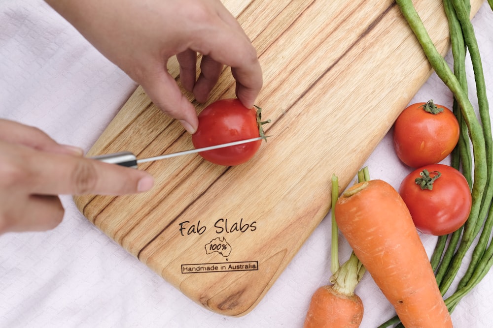 a person cutting tomatoes and carrots on a cutting board