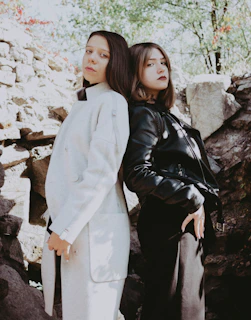 Two models wearing complementary streetwear outfits, standing back to back against a clean white wall.