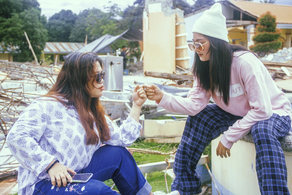 two women sitting on a wall and one of them is holding something