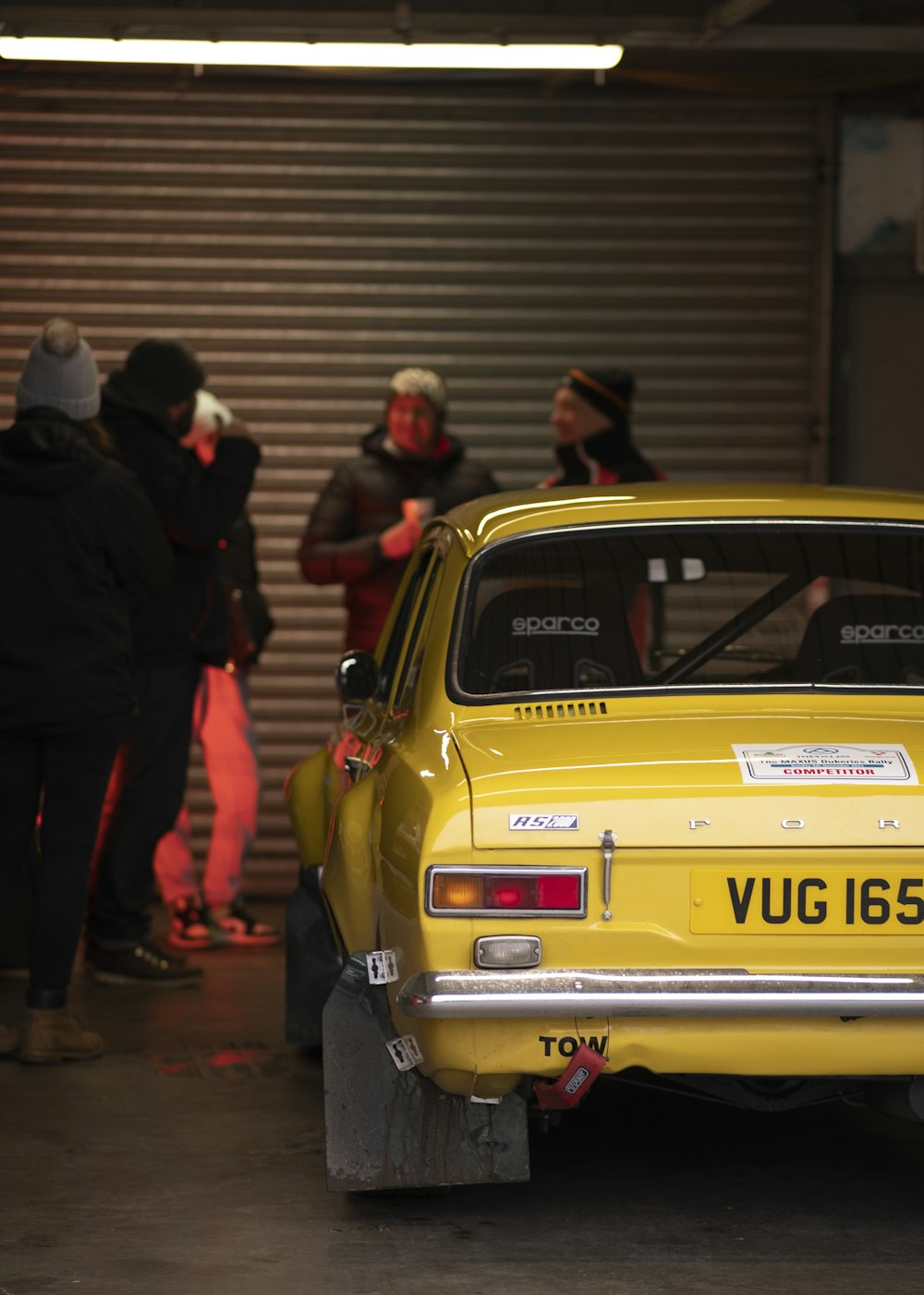 a group of people standing around a yellow car