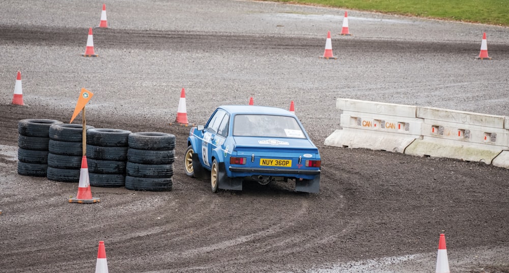 a small blue car driving around some orange cones