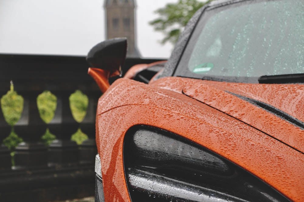 an orange sports car parked in front of a black fence