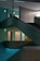 A multi-level interior space features intersecting staircases and illuminated exit signs, creating a geometric architectural design. The ambient lighting is dim, with turquoise hues casting a serene atmosphere across concrete textures.
