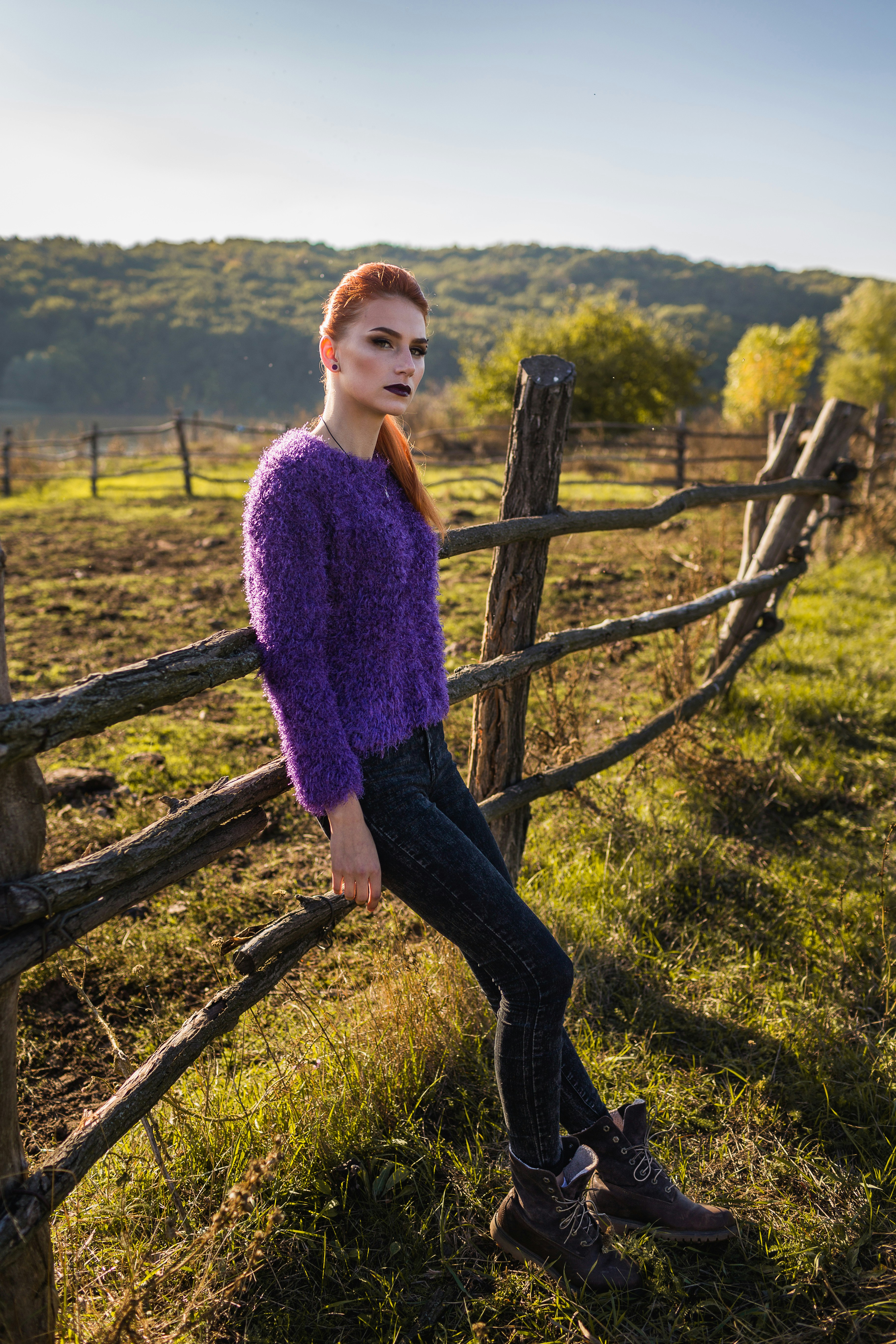 a woman in a purple sweater leaning on a fence