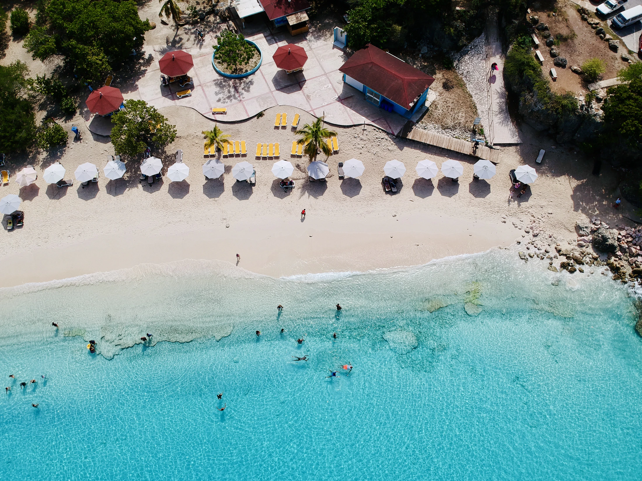 Aerial view of a clear-water beach with umbrellas and chairs