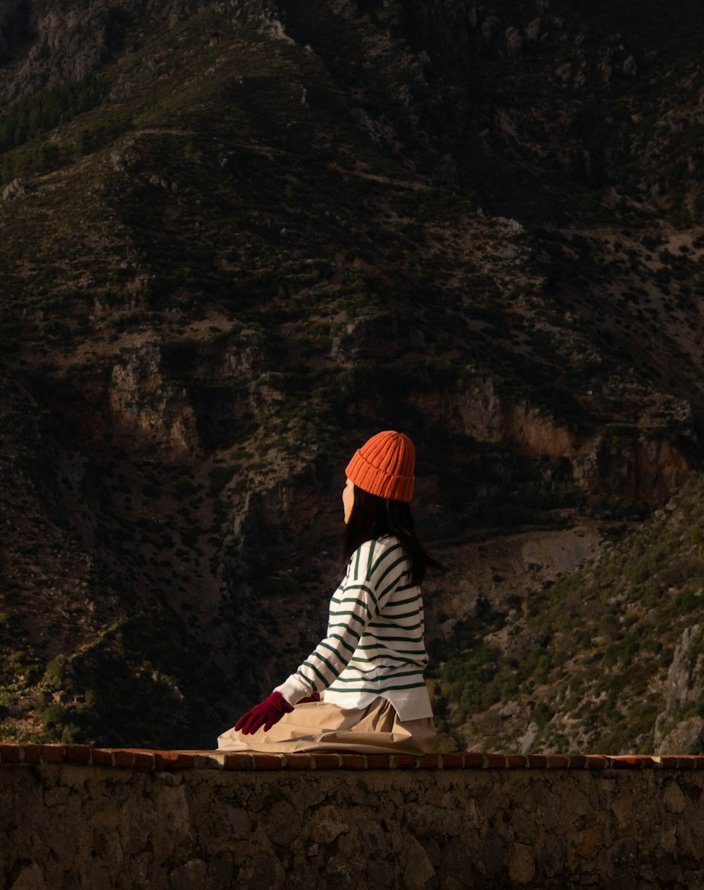 a woman sitting on a ledge with a mountain in the background