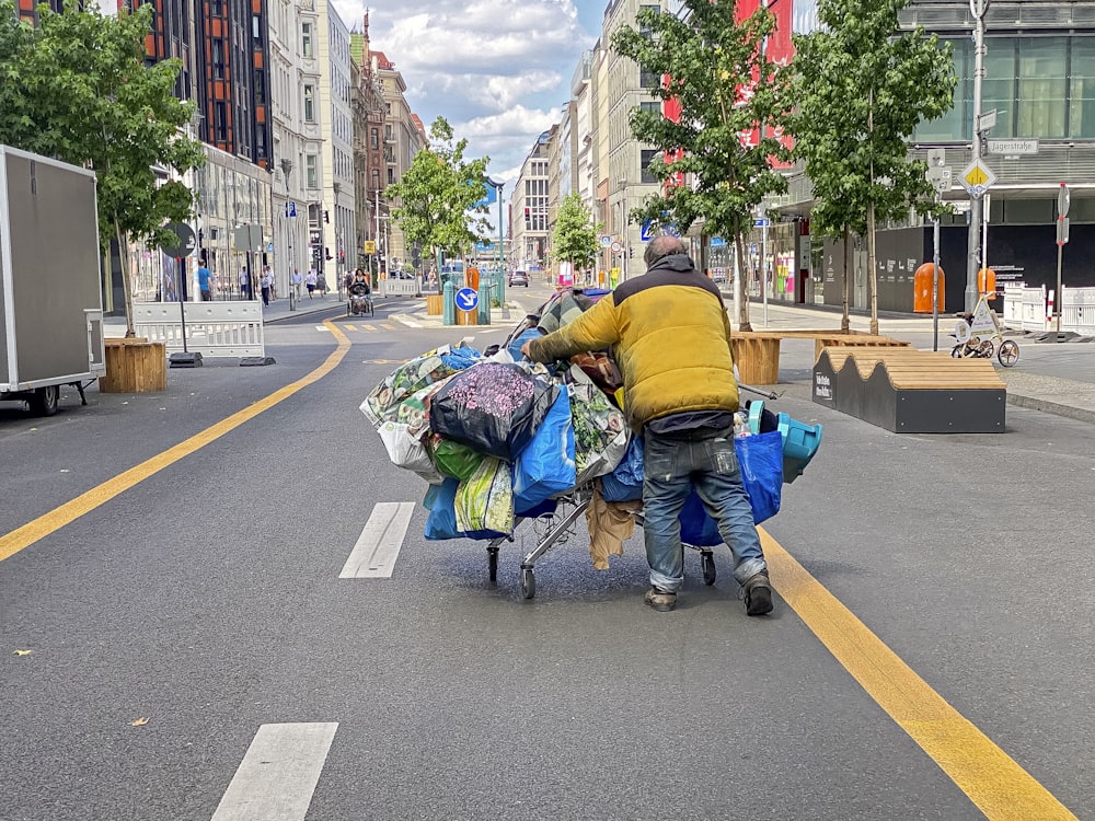 a man pushing a cart full of bags down a street