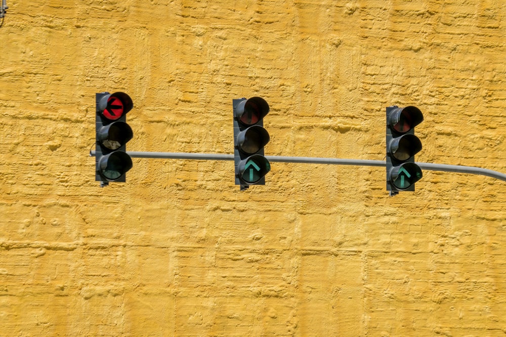 three traffic lights on a pole against a yellow wall