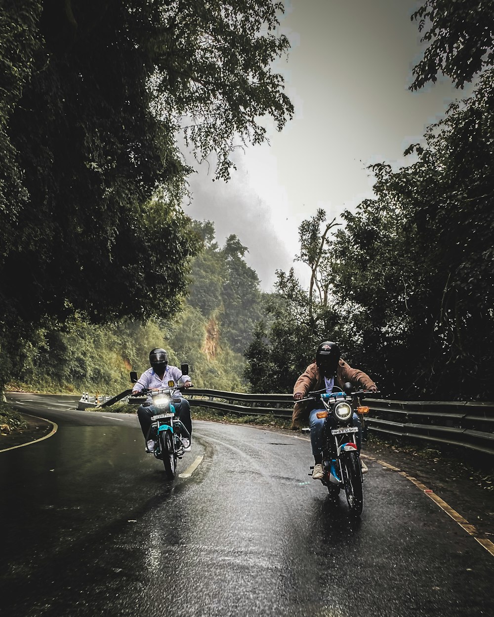 two people riding motorcycles on a wet road