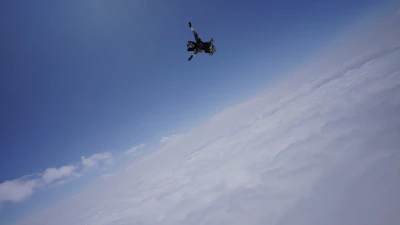 Close-up of a skydiver checking their altimeter against a backdrop of blue sky and clouds.