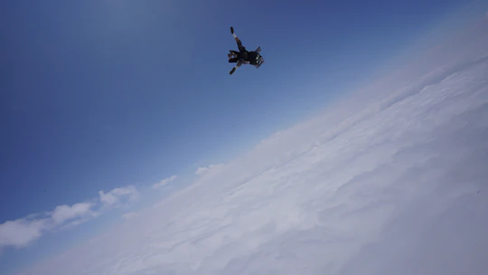 A vibrant skydiver in freefall against a bright blue sky with scattered clouds.