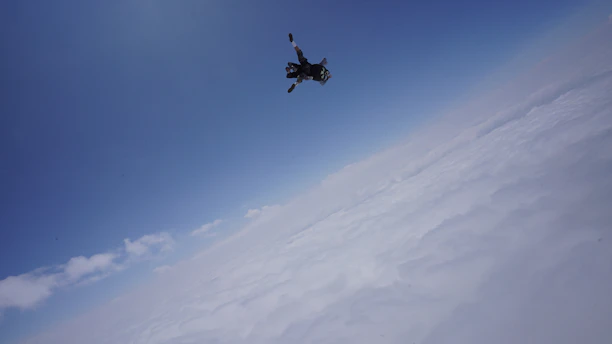 A vibrant skydiver in freefall against a bright blue sky, with a subtle overlay of an altimeter graphic.