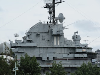 A large, gray naval battleship is pictured, featuring radar and communication equipment on its upper structure. The ship