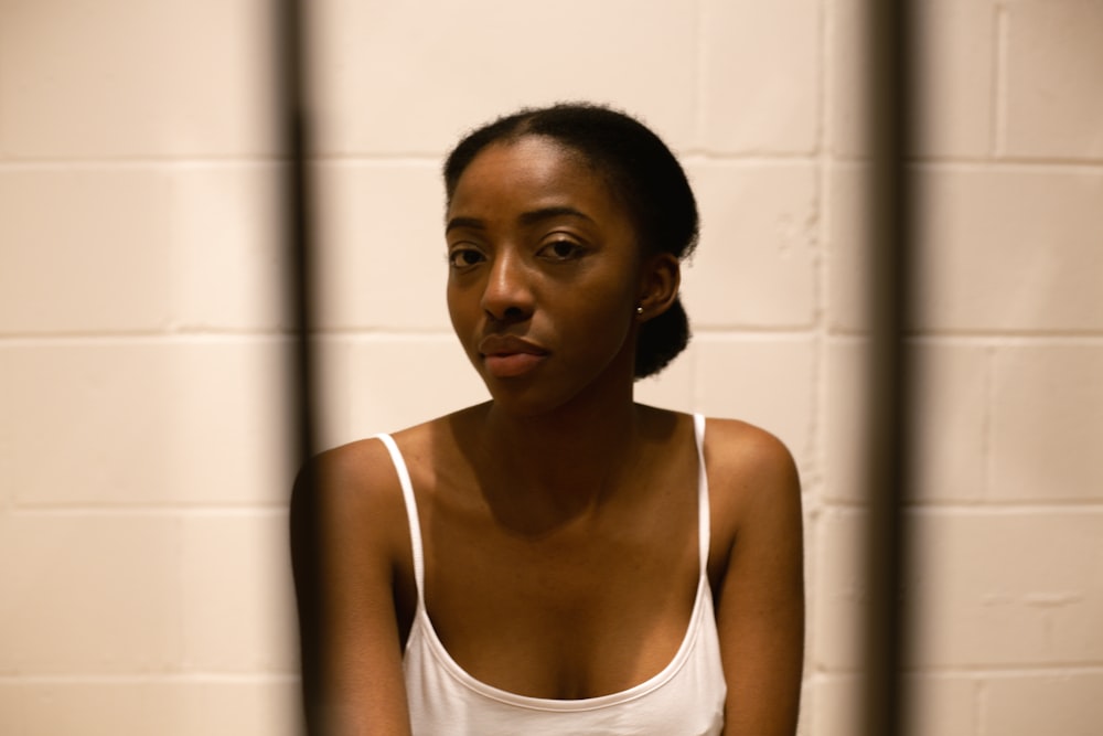 a woman in a white tank top sitting in a jail cell