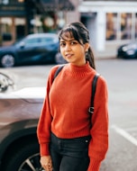 a woman standing in front of a car wearing a red sweater