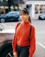 a woman standing in front of a car wearing a red sweater
