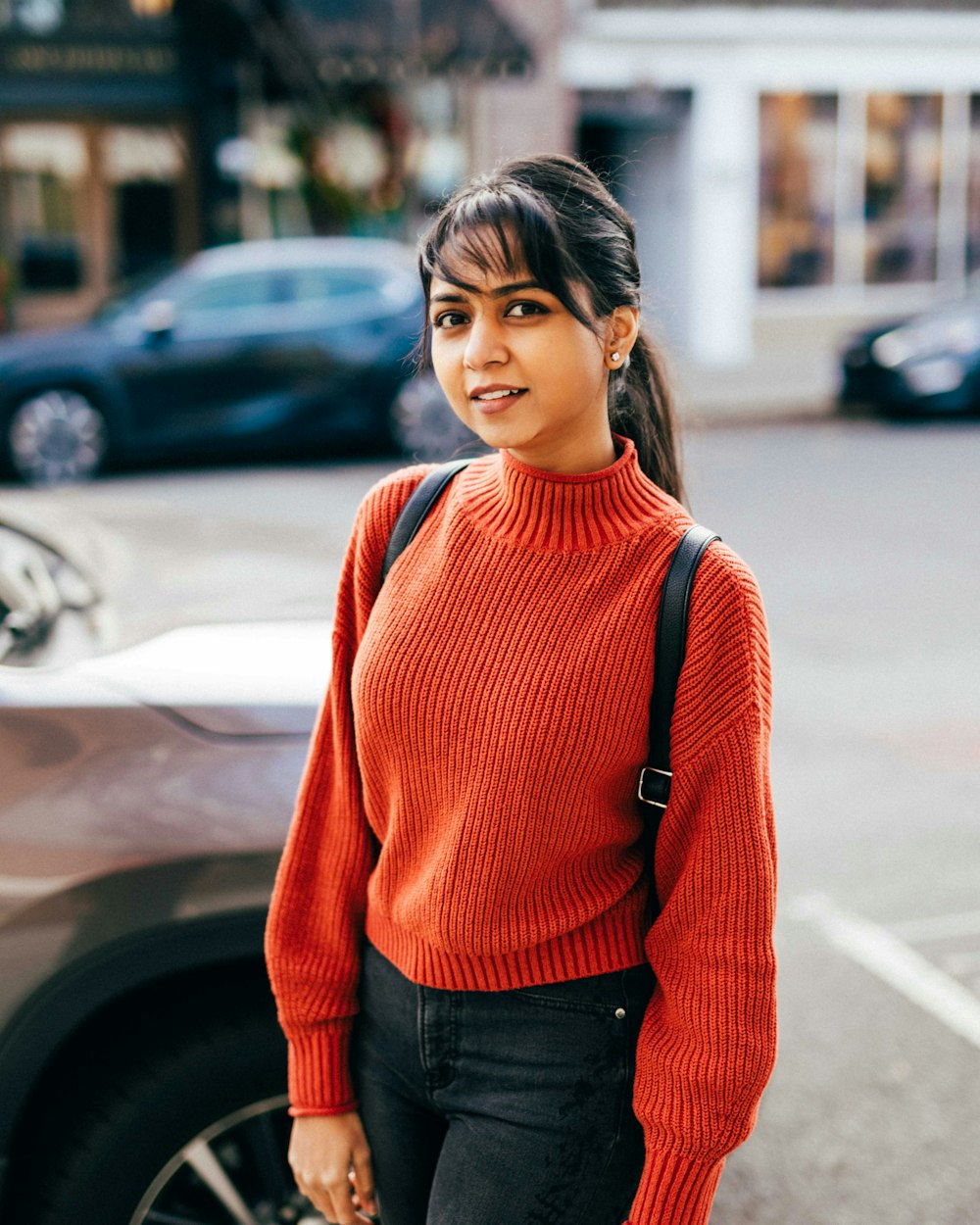 a woman standing in front of a car wearing a red sweater