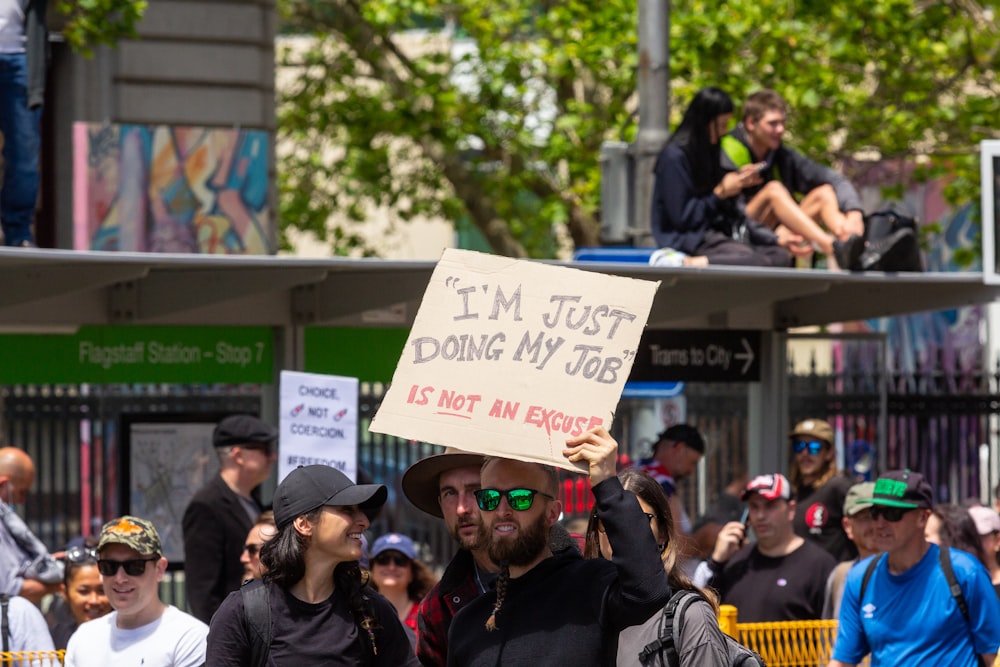 a man holding a sign that says i'm just doing my job