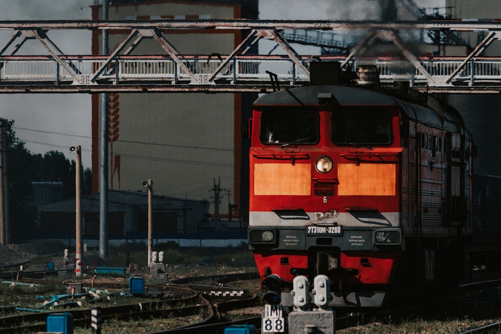 a red train traveling down train tracks under a bridge