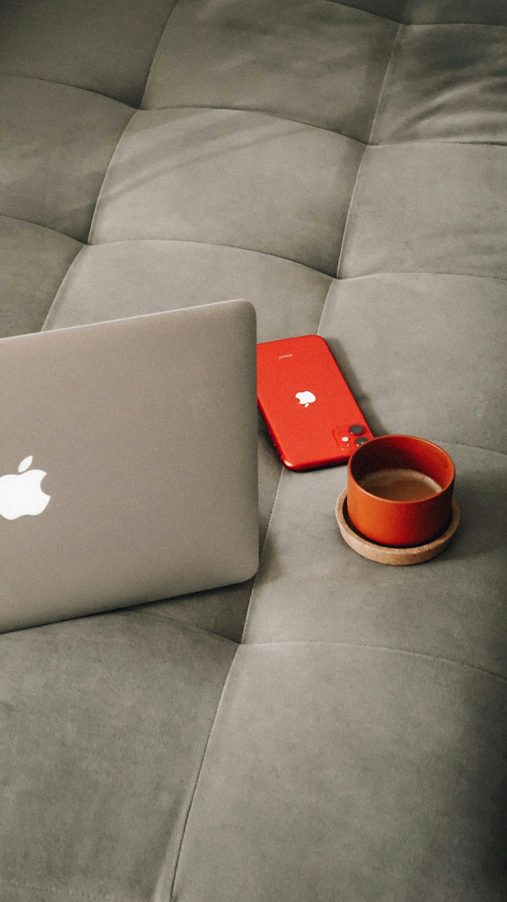 an apple laptop sitting on a couch next to a cup of coffee