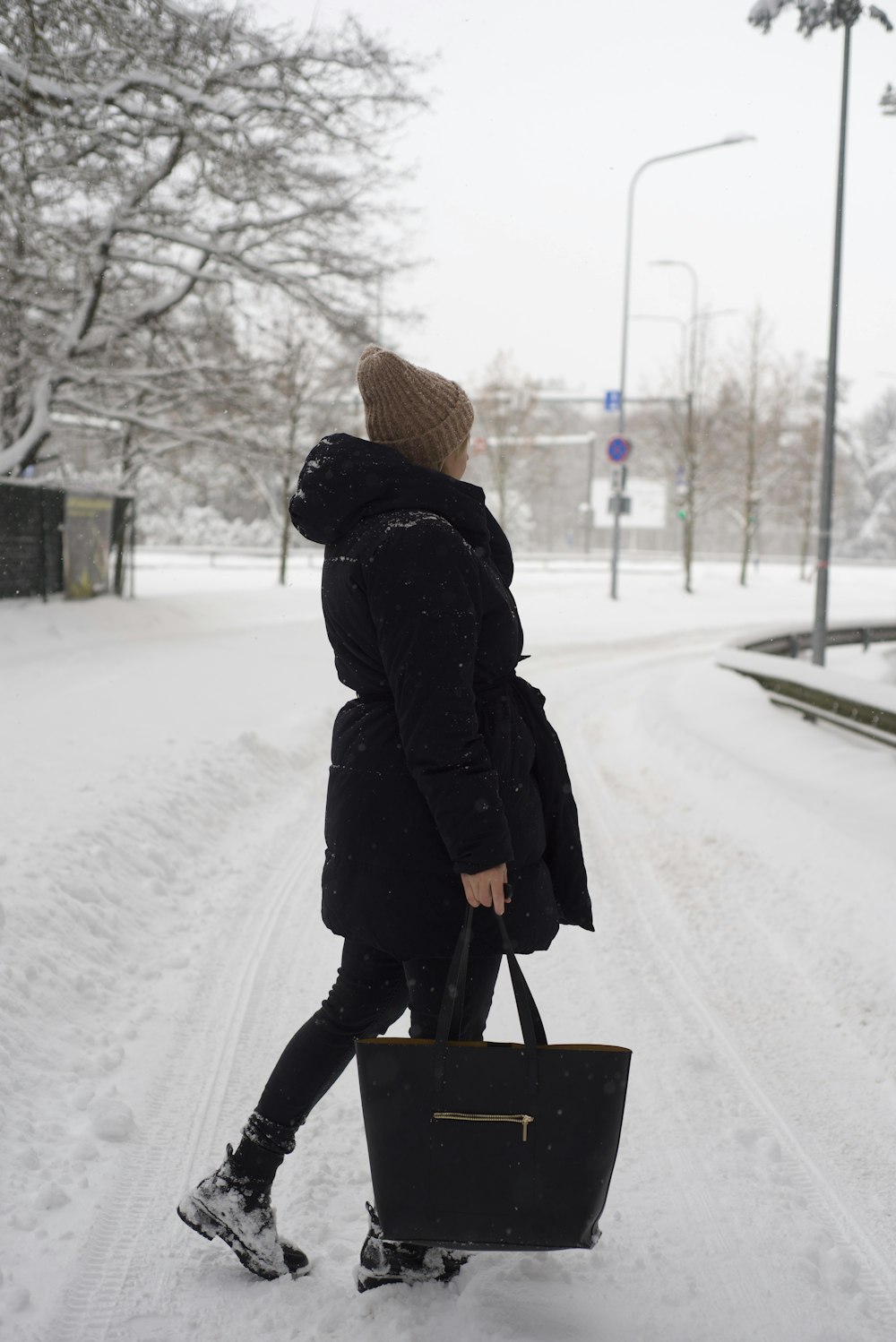 a woman walking in the snow carrying a black bag