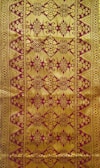 Intricate textile design featuring ornate golden patterns on a reddish-brown background, with symmetrical, repetitive motifs that include floral and geometric elements.