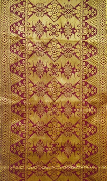 Intricate textile design featuring ornate golden patterns on a reddish-brown background, with symmetrical, repetitive motifs that include floral and geometric elements.