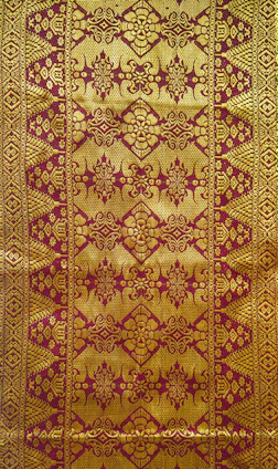 A colorful Patola silk textile featuring traditional geometric and floral patterns with rich reds, blues, and gold accents.