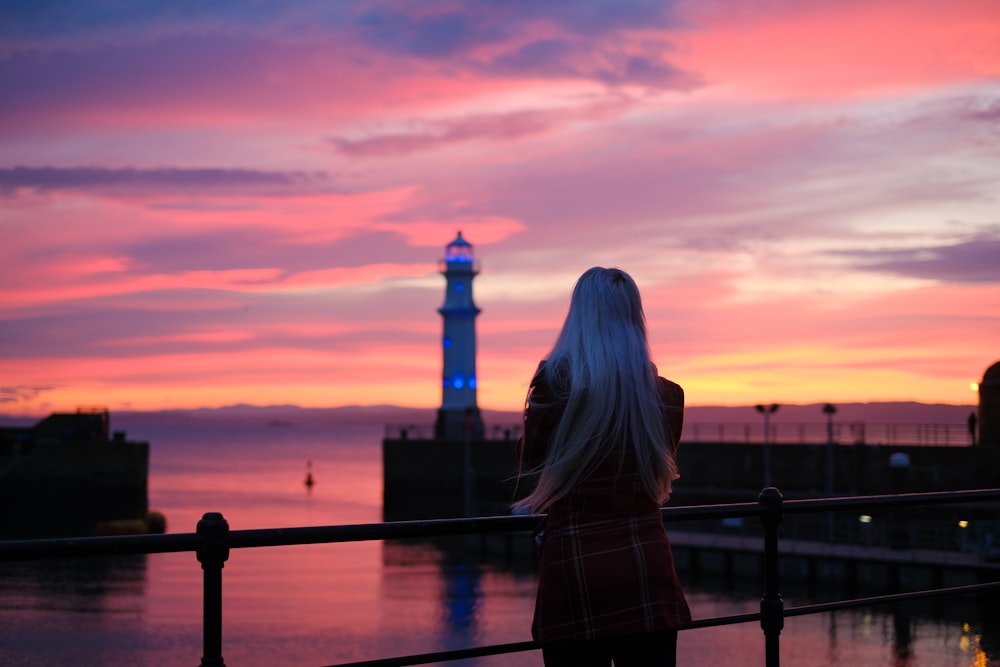 a woman standing on a railing looking at a lighthouse